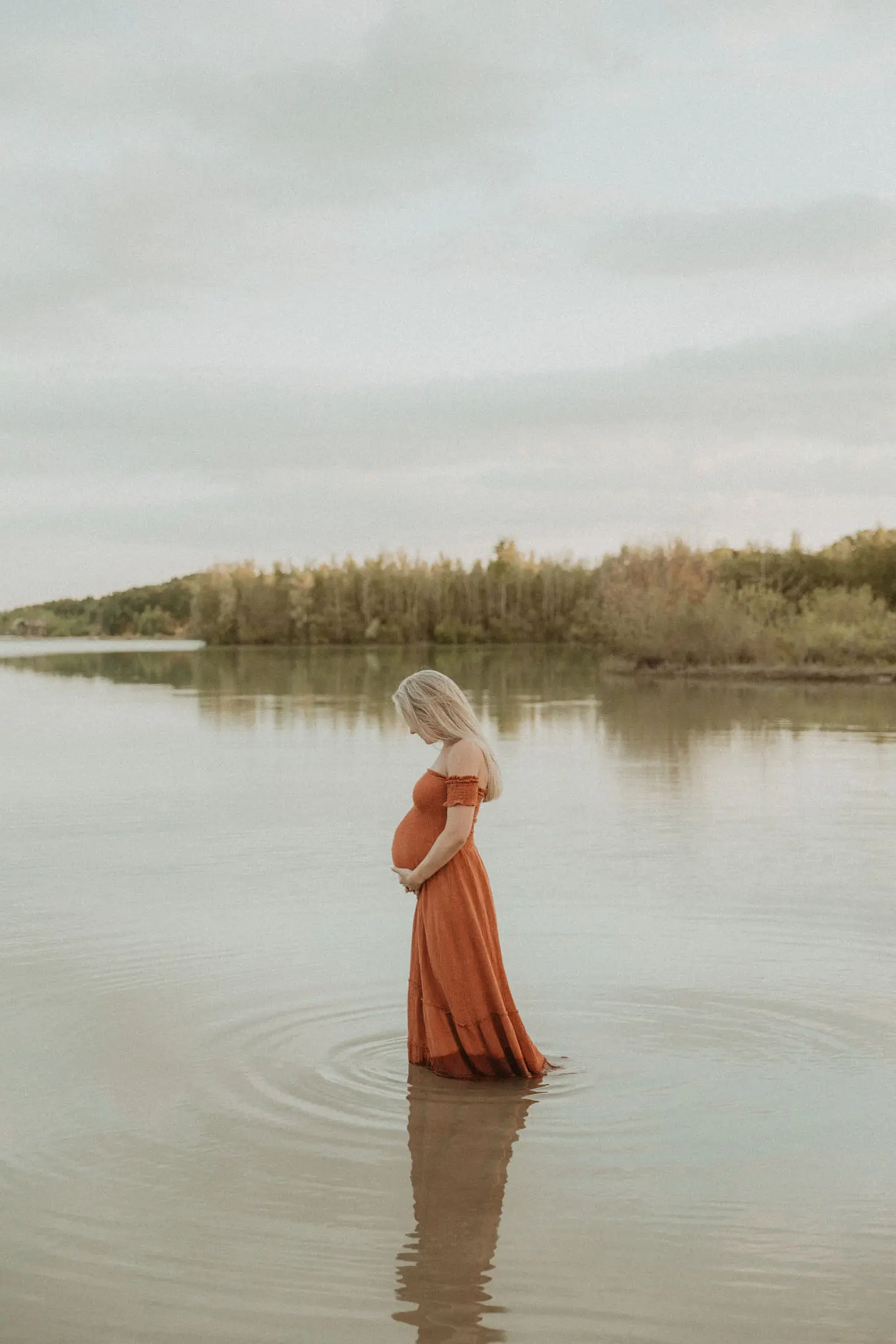 Zwangere vrouw staat in profiel aan het water